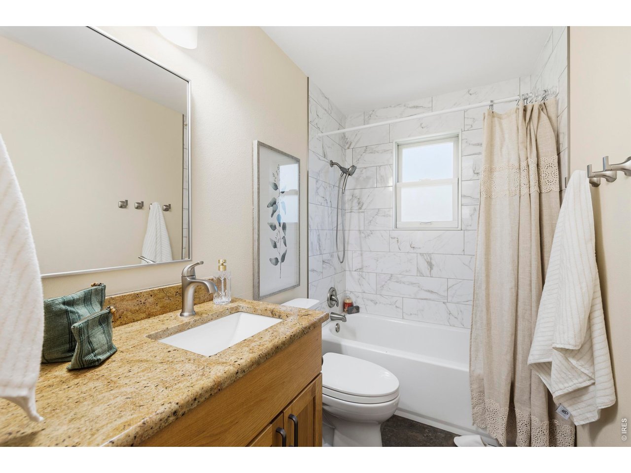 Bathroom with a marble-look tiled tub and shower, window, and wood vanity with granite countertop.