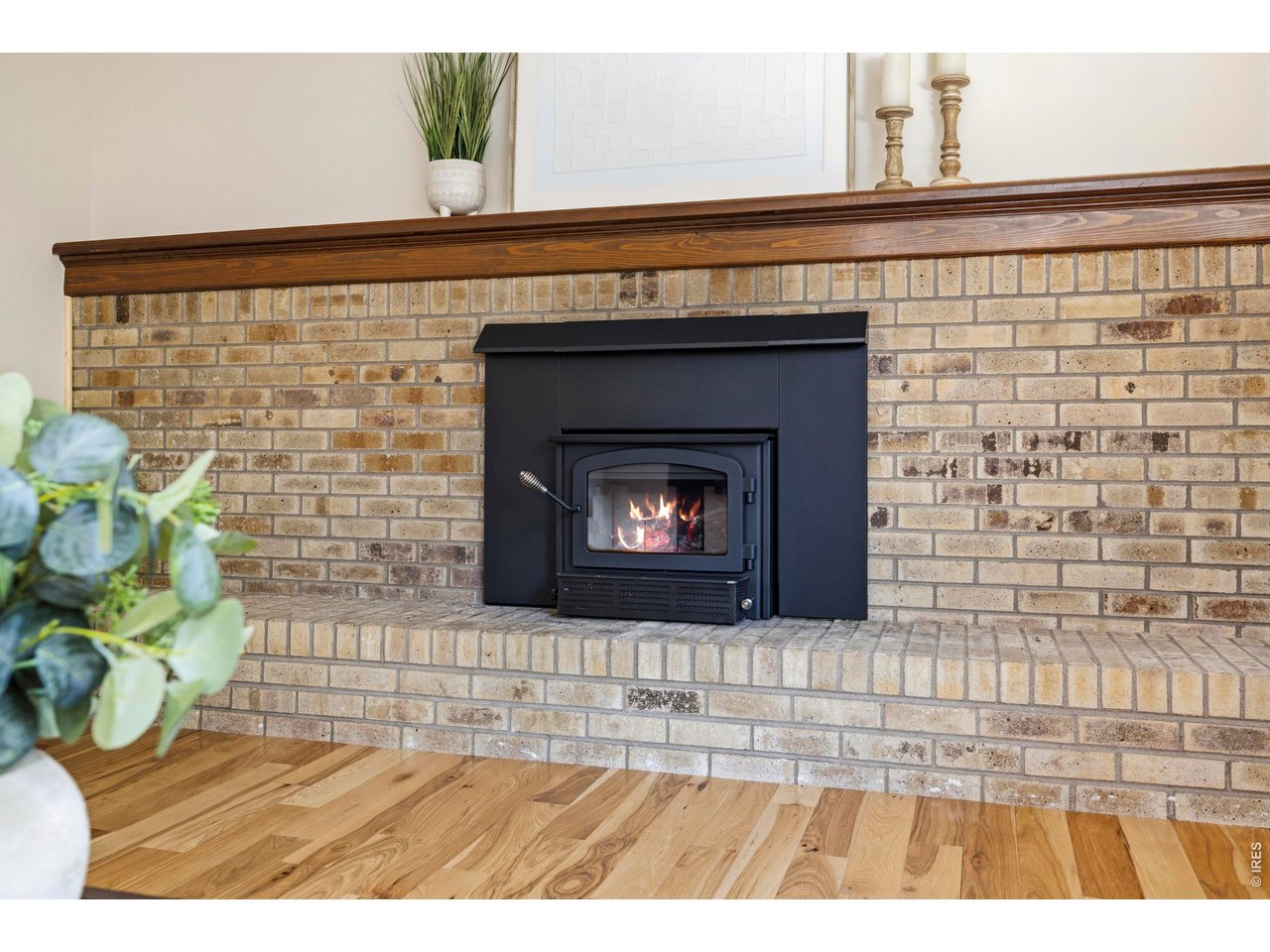 Brick fireplace with a black stove insert, visible fire, and dark wood mantel.
