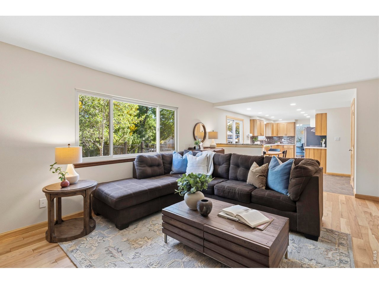 Furnished living room with a dark sectional, large windows, and an open connection to the kitchen.