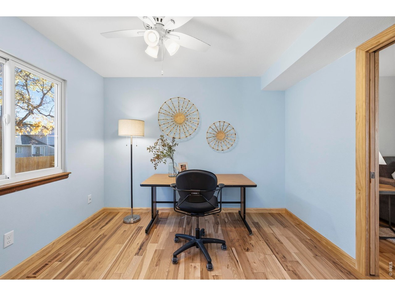 Home office with a desk and rolling chair, pale blue walls, and wood flooring.