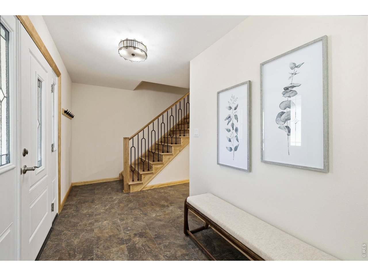 Entryway with a glass-panel front door, tiled floor, and wood staircase with black railing.