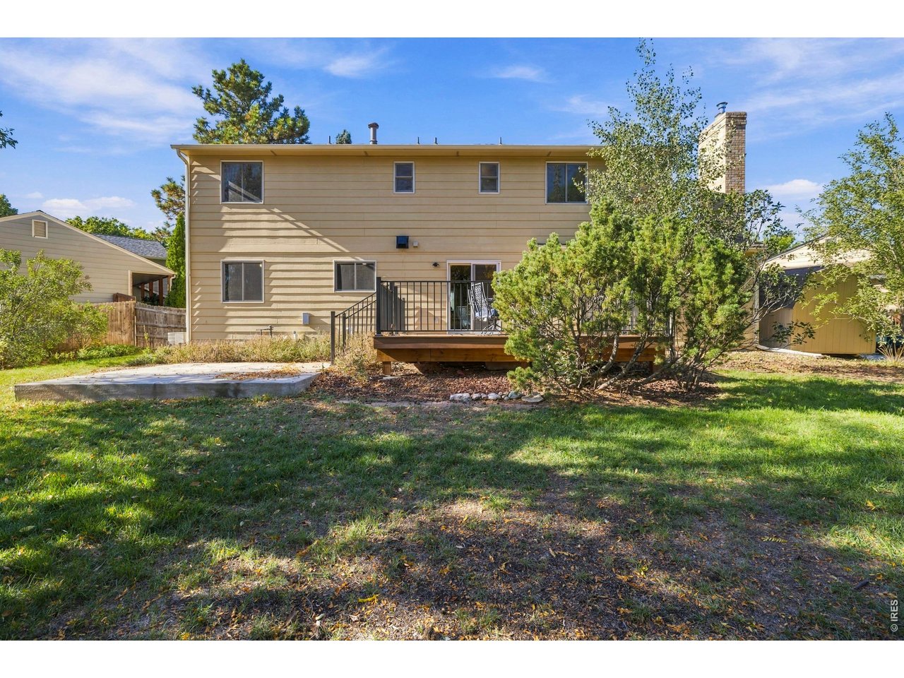 Two-story tan house with a raised rear deck, brick chimney, and tree-shaded lawn.