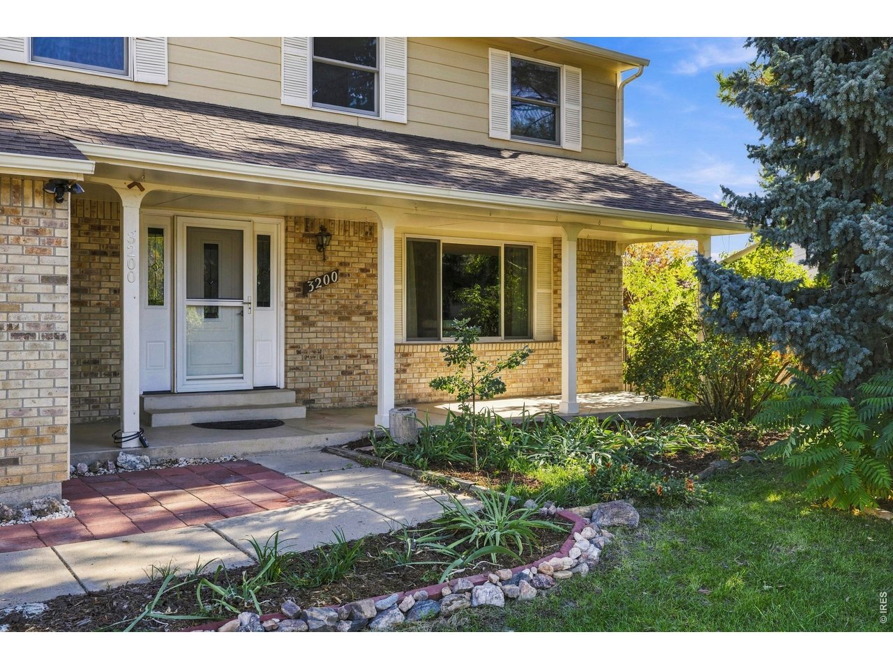 Two-story home with a brick facade, covered porch, and landscaped front garden.