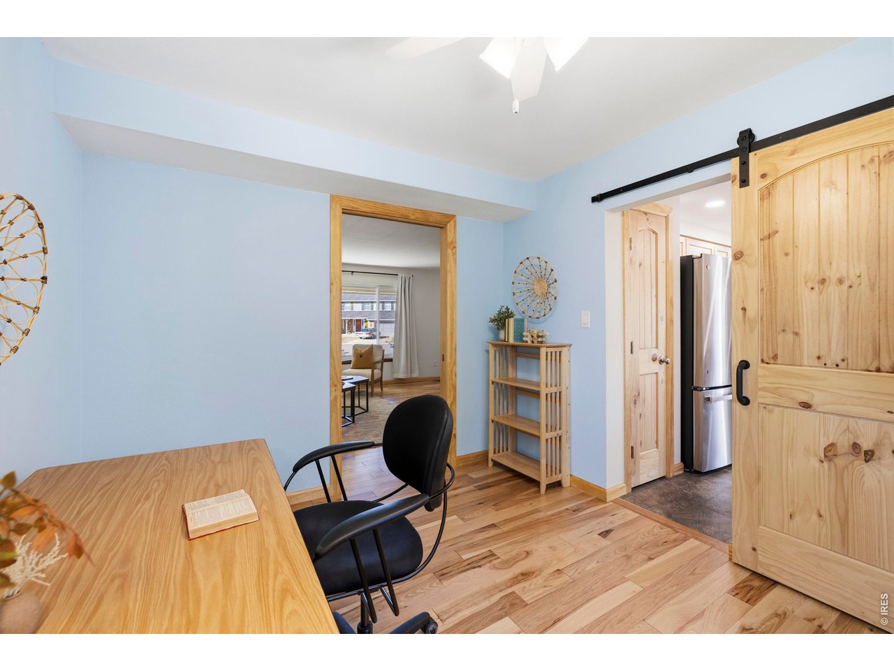 Home office with a light wood desk and black chair beside a natural wood sliding barn door.