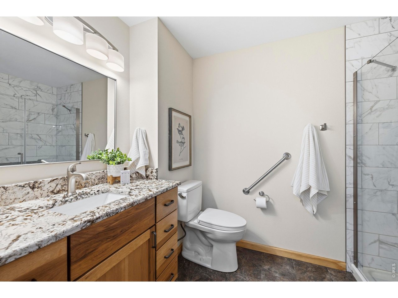 Bathroom with a granite-topped wood vanity, marble-look shower tile, and grab bars.