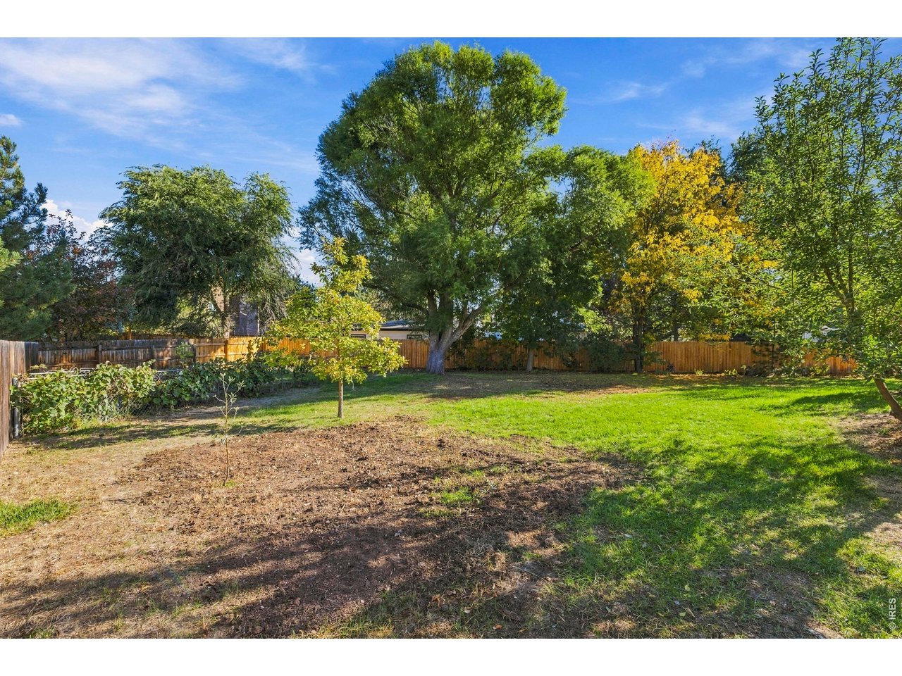 Fenced backyard with a broad lawn, mature trees, and garden beds.