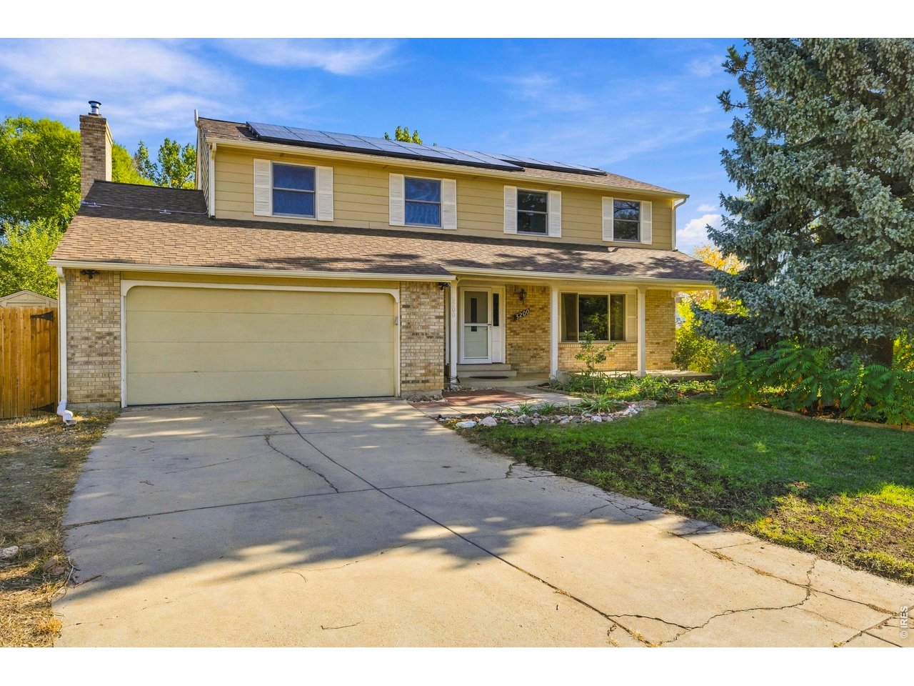 Two-story yellow-and-brick house with rooftop solar panels, attached garage, and broad concrete driveway.