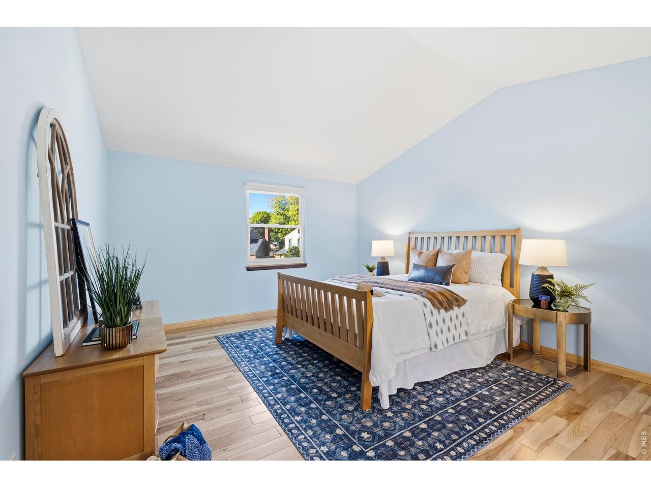 Staged bedroom with a wooden bed, pale blue walls, and a blue patterned rug.
