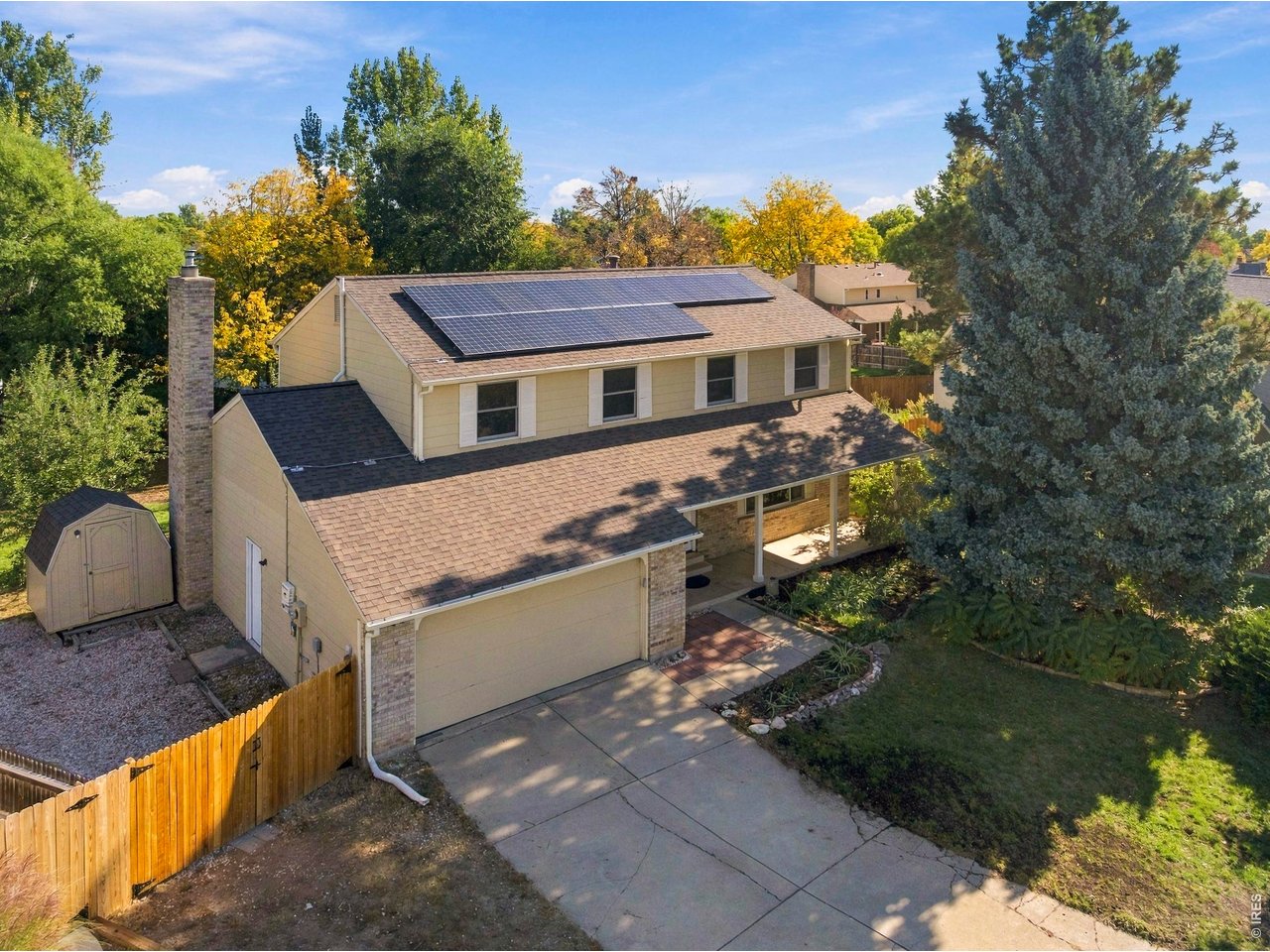 Two-story beige home with rooftop solar panels, an attached garage, and a backyard shed.