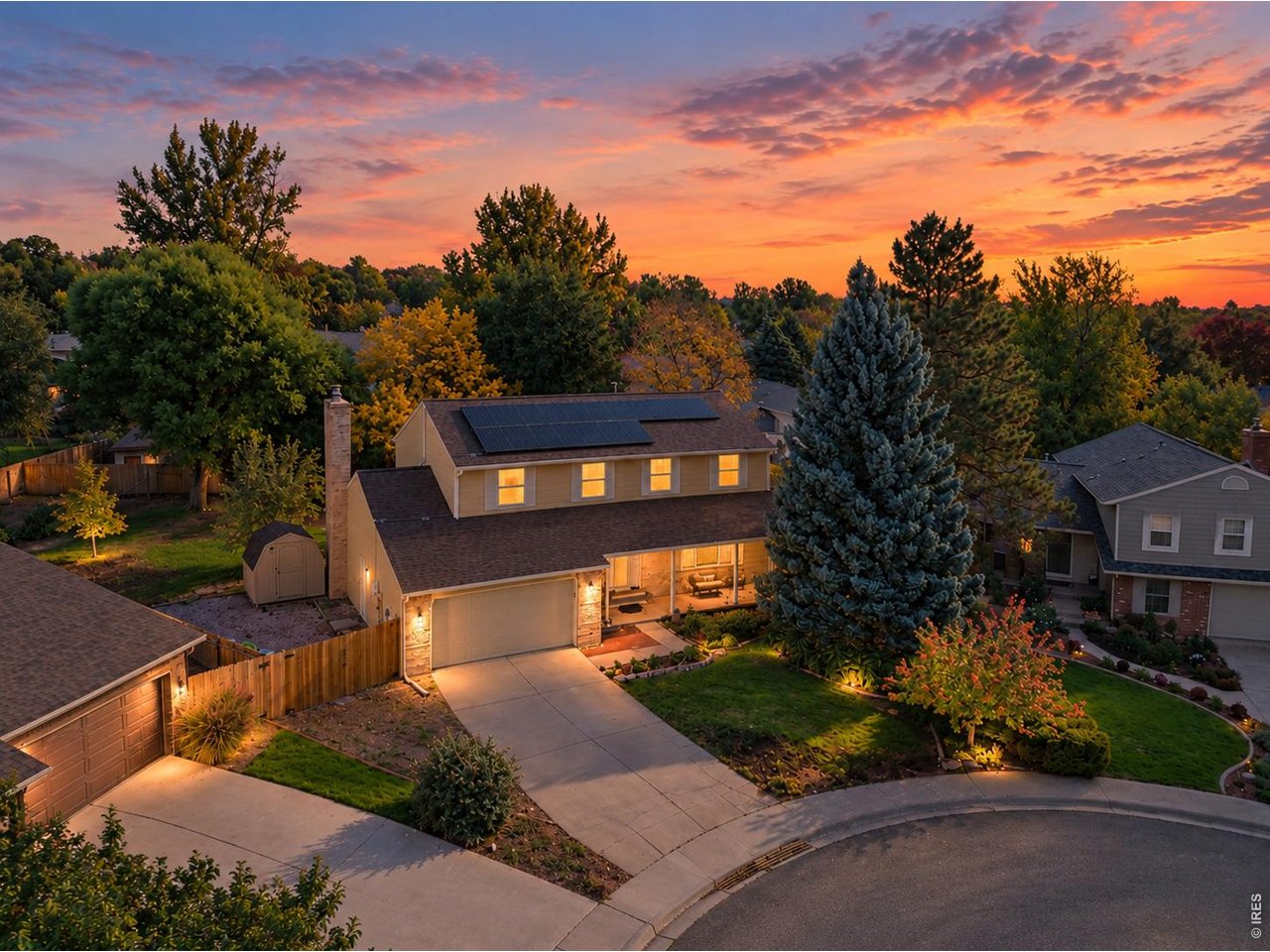 Two-story home with rooftop solar panels and landscaped yard at sunset.