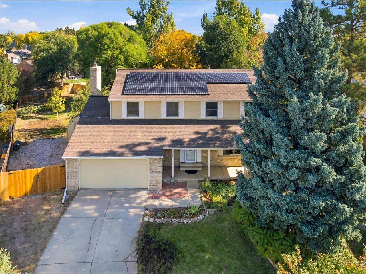 Two-story house with rooftop solar panels, a front driveway, and a large evergreen tree.
