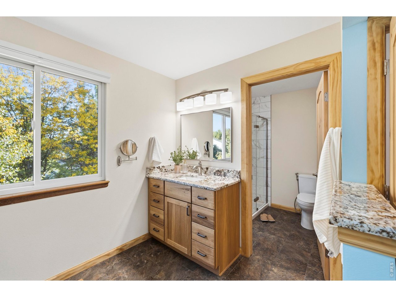 Bright bathroom with a wood vanity, large window, and tiled glass shower.