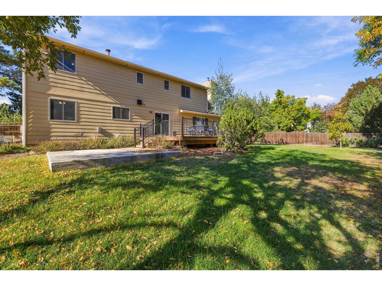 Rear of a two-story tan home with a raised deck overlooking a fenced, leafy backyard.
