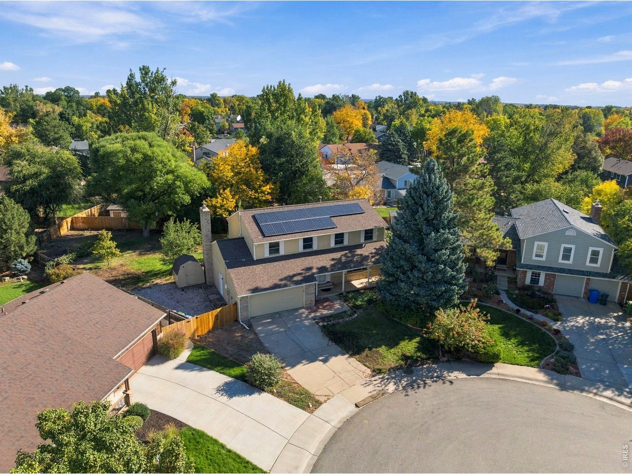Aerial view of a two-story home with rooftop solar panels and autumn trees.