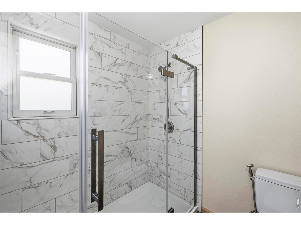Bathroom shower with marble-look tile, glass enclosure, and window.