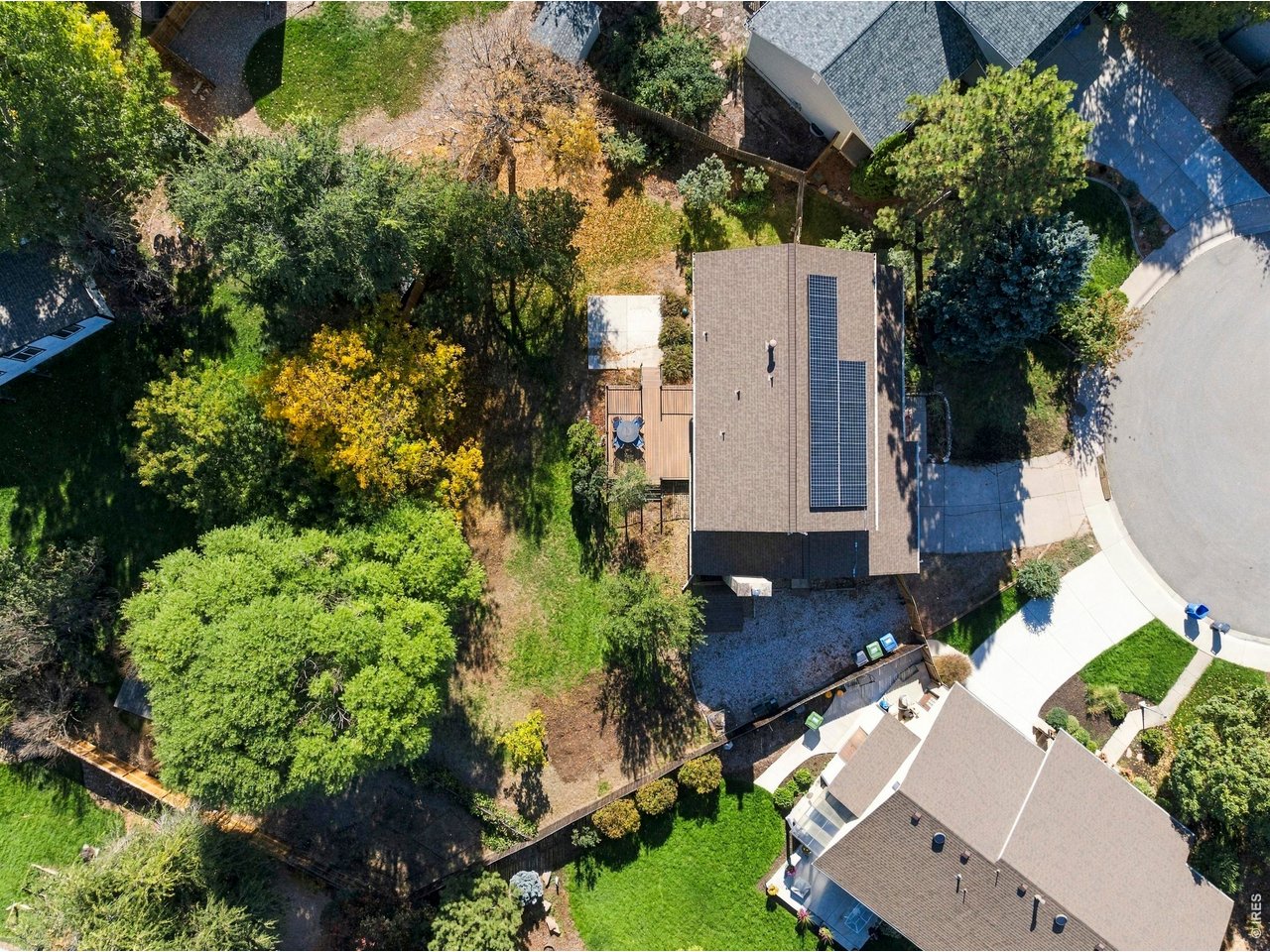 Aerial view of a home with rooftop solar panels, a fenced backyard, and mature trees.