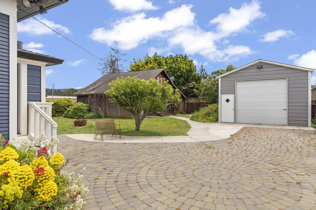 Backyard with a paved courtyard, flowering garden, lawn, wooden shed, and detached garage.