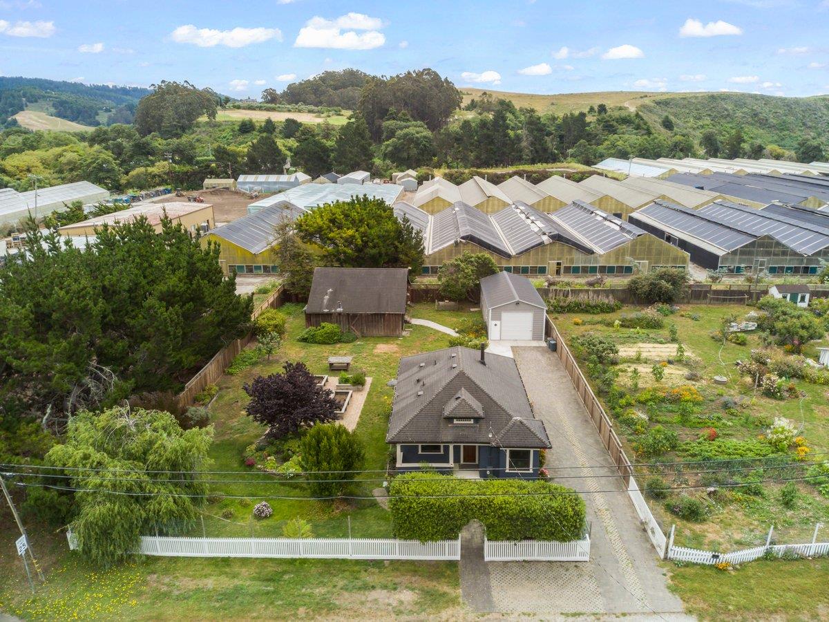 Aerial view of a house with a fenced garden and detached shed, beside rows of greenhouses.