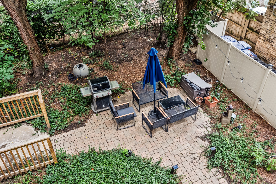 Backyard patio with brick pavers, outdoor seating, a blue umbrella, and a gas grill.
