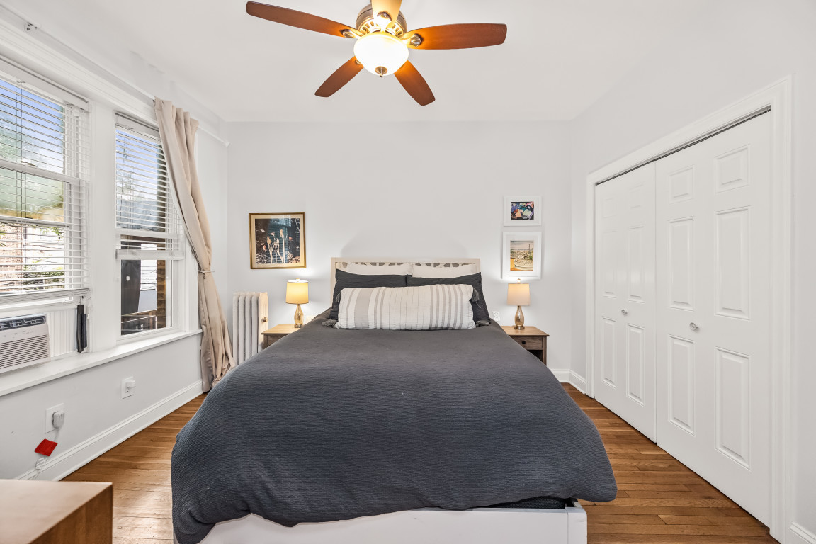 Bedroom with a dark gray bed, tall curtained windows, hardwood floors, and white closet doors.