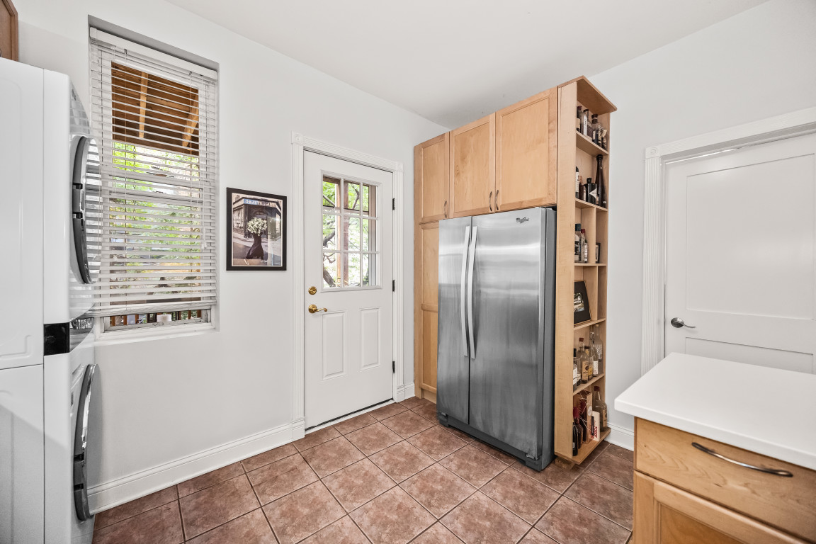 Kitchen with light wood cabinetry, stainless steel refrigerator, and tiled floor.