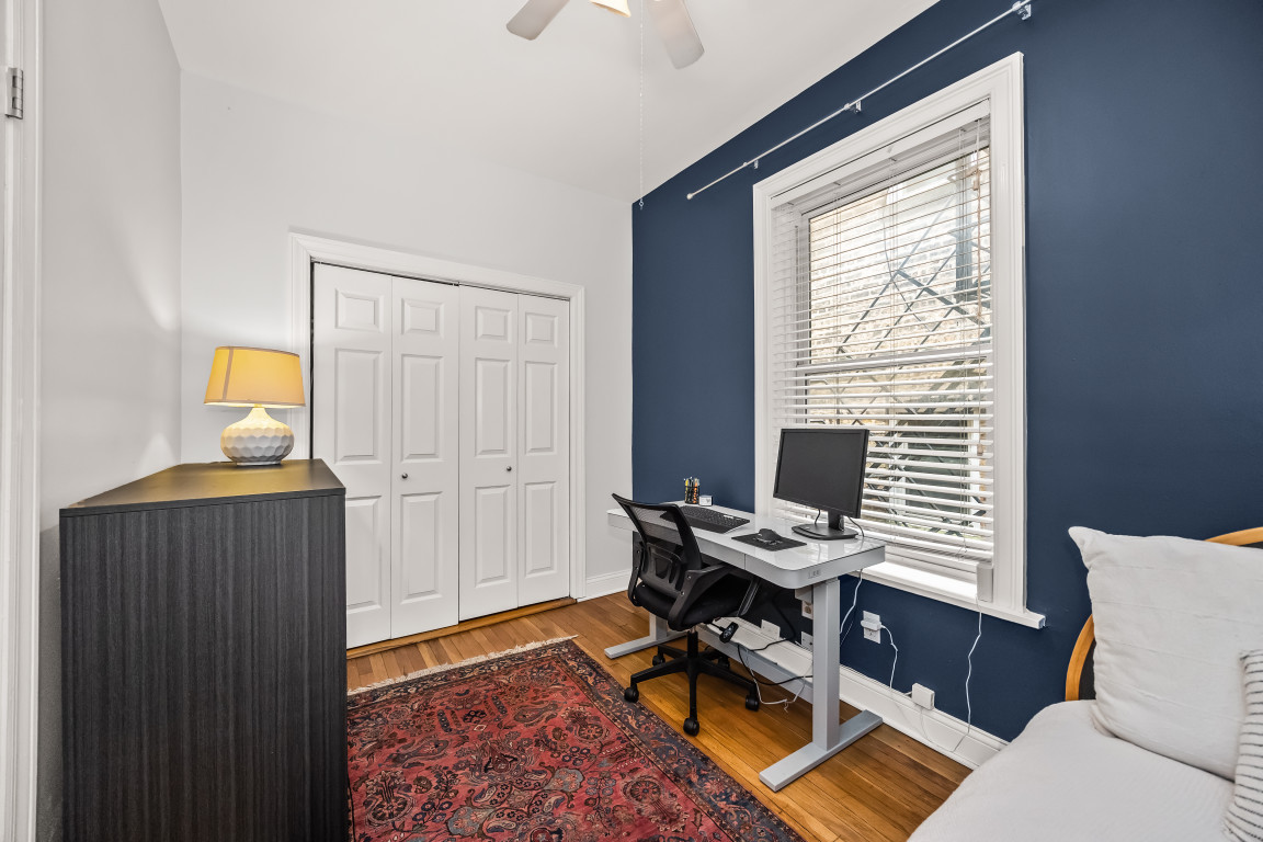 Bedroom with a desk and computer beside a window, white closet, and dark blue accent wall.