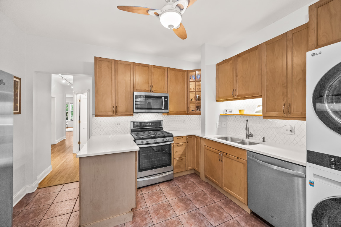 Kitchen with warm wood cabinets, white counters, stainless steel appliances, and reddish-brown tile flooring.