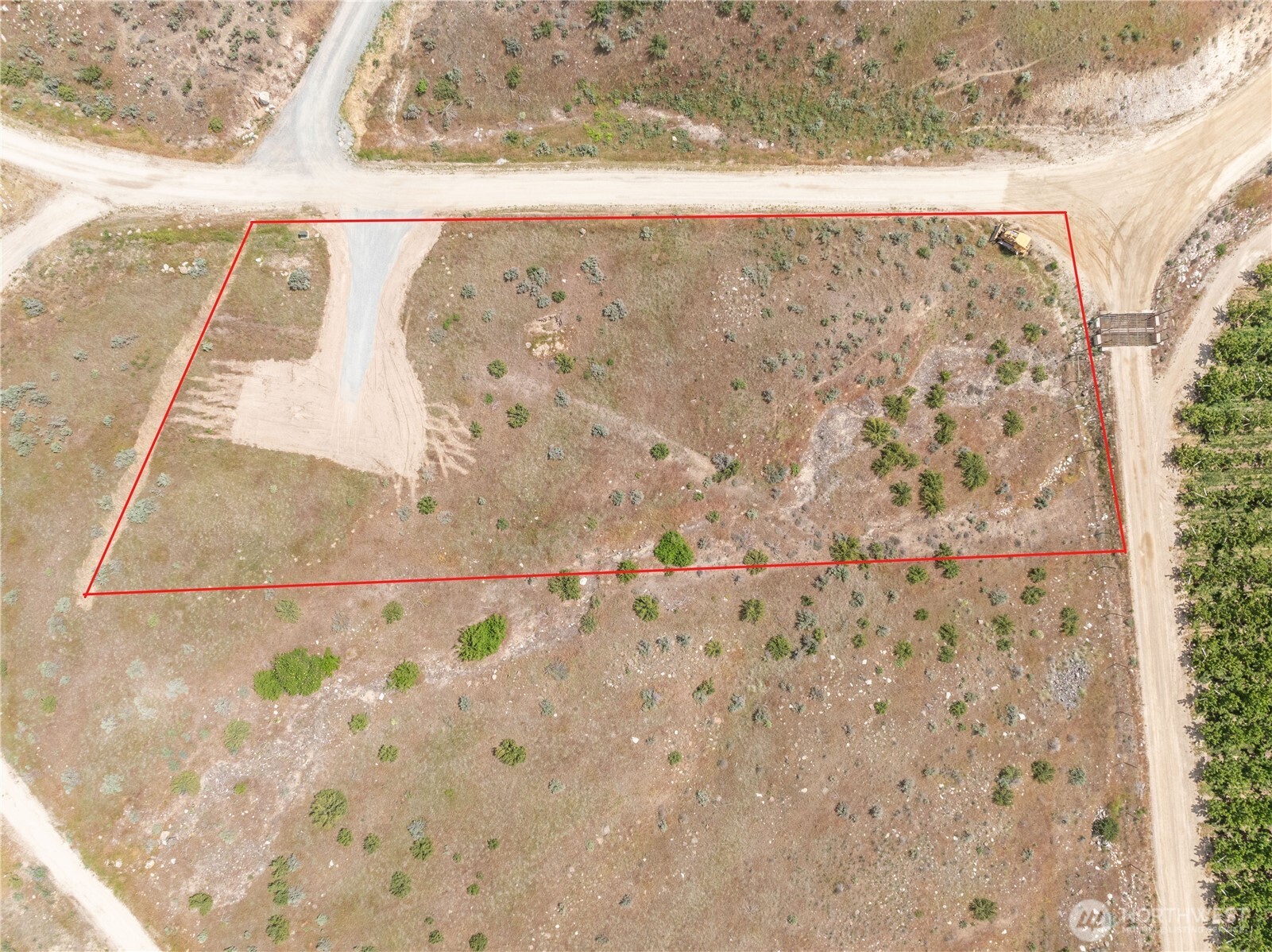 Aerial view of a dry, shrub-covered vacant lot outlined in red beside unpaved roads.