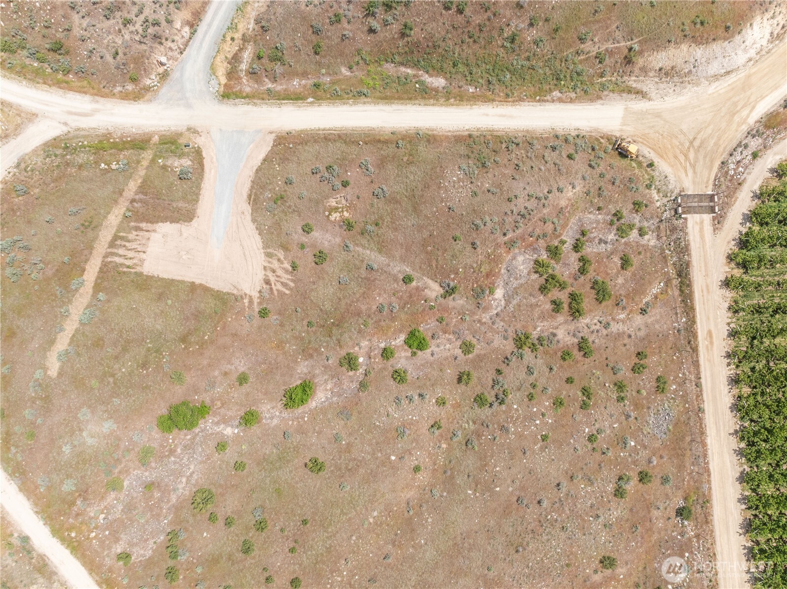 Aerial view of a scrub-covered vacant parcel bordered by unpaved roads, with a small construction vehicle nearby.