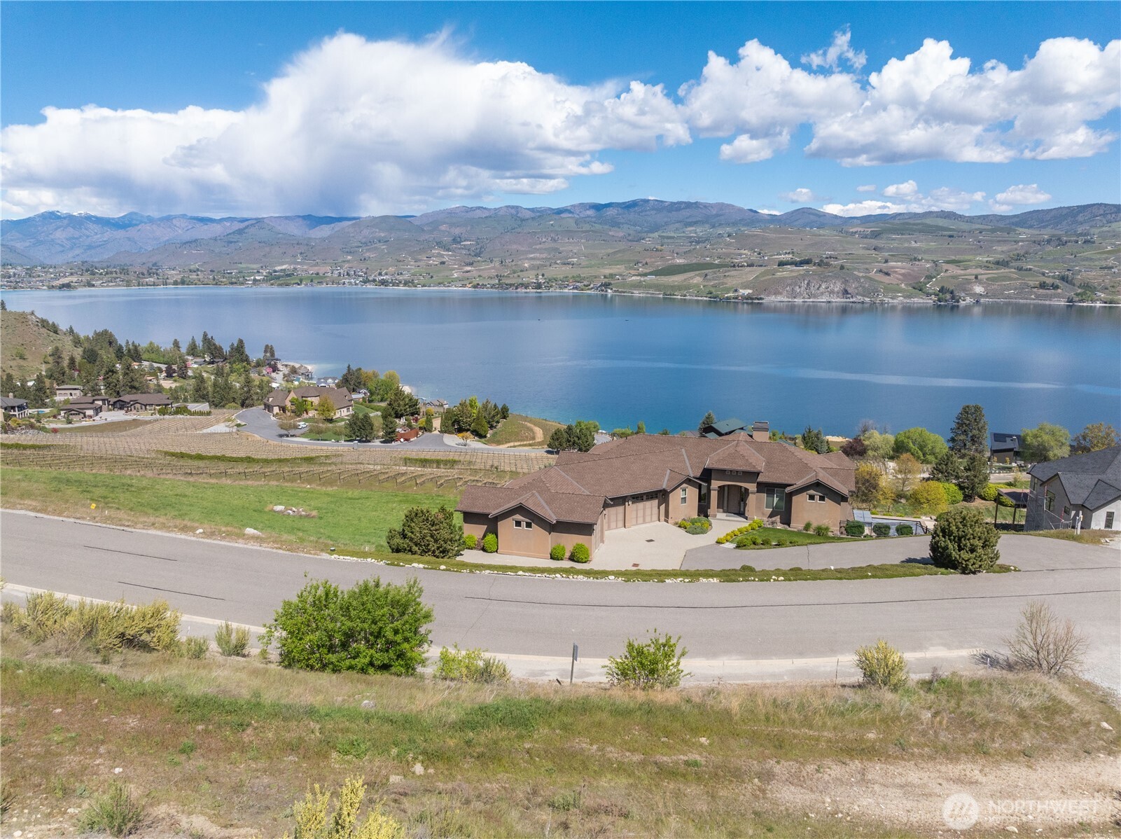 Hillside home above Lake Chelan, with vineyard rows and mountain views.