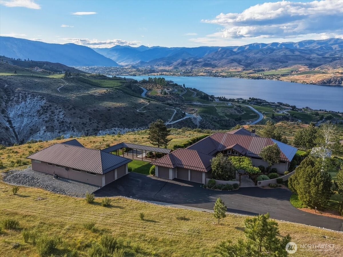 Hillside home above Lake Chelan, with brown metal roofs, mountain views, and landscaped grounds.