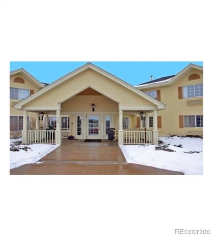 Pale-yellow building with a covered central entrance, white porch railings, and snow along the walkway.