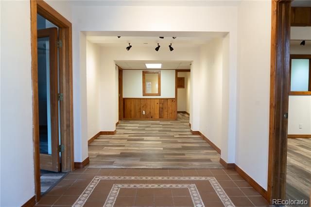 Empty lower-level hallway with wood-look flooring, brown tile entry, and wood-trimmed doorways.