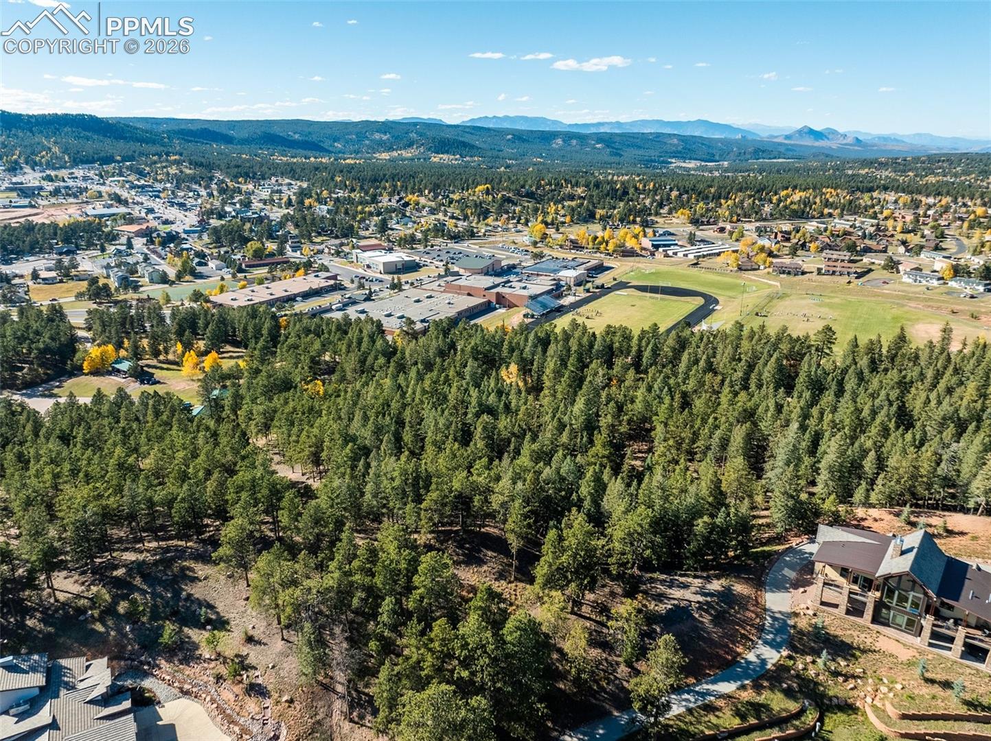 Aerial view of a wooded property with a home, nearby town, and distant mountain ranges.