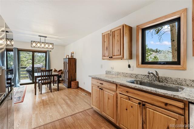 Kitchen with knotty wood cabinets and granite counters, adjoining dining area beside sliding glass doors to trees.