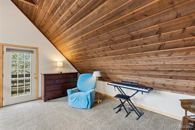 Furnished attic room with a sloped wood ceiling, blue armchair, and electronic keyboard.