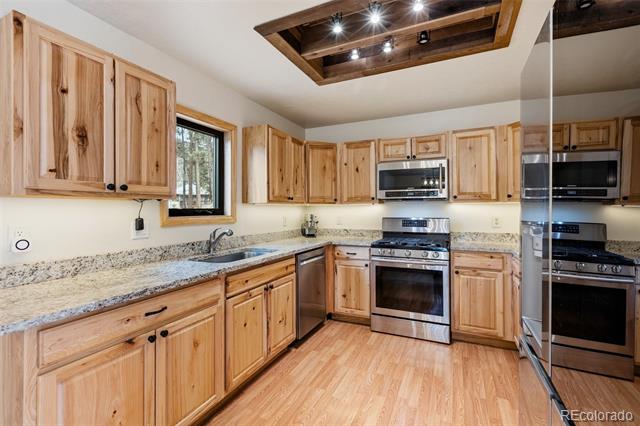 Kitchen with natural wood cabinets, stone counters, stainless appliances, and a recessed wood ceiling feature.