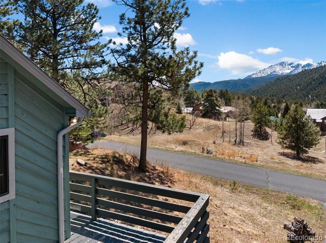 Deck beside a blue-sided home overlooking pine-covered hills and snow-capped mountains.