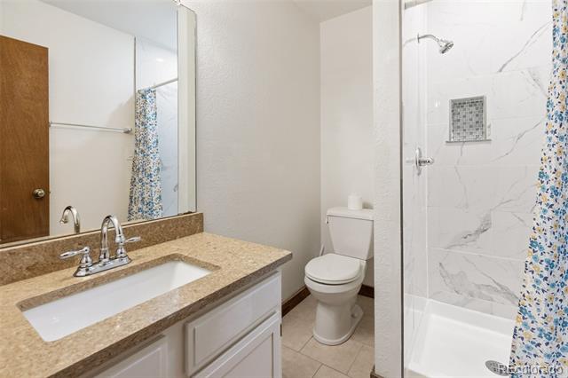 Bathroom with a white vanity, large mirror, toilet, and marble-look shower with a blue floral curtain.