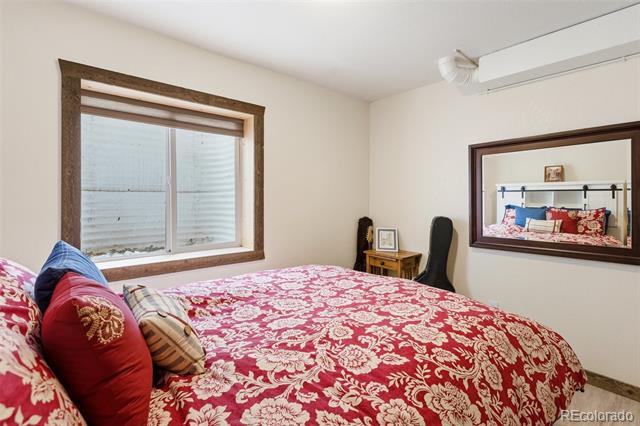 Bedroom with a red floral bedspread, wood-trimmed window, and wall mirror.