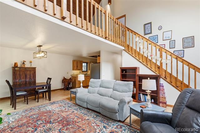 Living room with gray sofa, patterned rug, and wooden staircase overlooking the dining area.