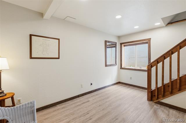 Mostly empty room with light wood-look flooring, two windows, and a wooden staircase.