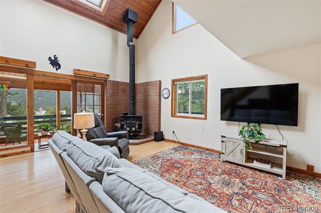 Living room with a vaulted wood ceiling, freestanding stove, sliding glass doors, and patterned rug.