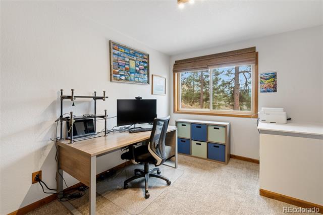 Home office with a wooden desk, computer, rolling chair, and window overlooking trees.
