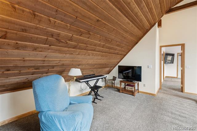Attic sitting room with a sloped wood ceiling, blue armchair, television, and desk.