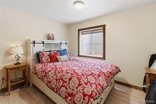 Bedroom with a red floral bedspread, wooden bedside tables, and a window with blinds.