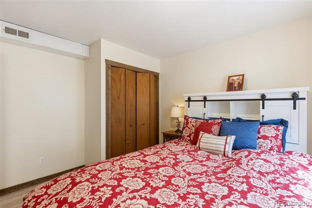 Bedroom with a red floral comforter, blue pillows, and wooden closet doors.