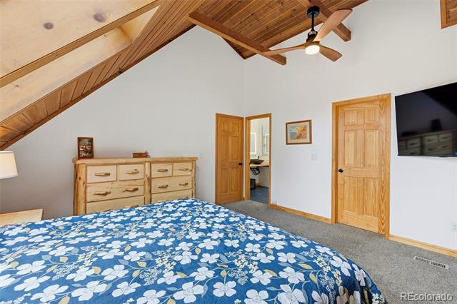 Bedroom with a blue floral bedspread beneath a vaulted, wood-beamed ceiling.