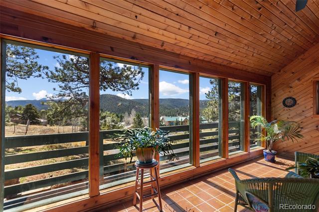 Sunroom with a vaulted wood ceiling, terracotta tile, and windows overlooking pine trees and mountains.