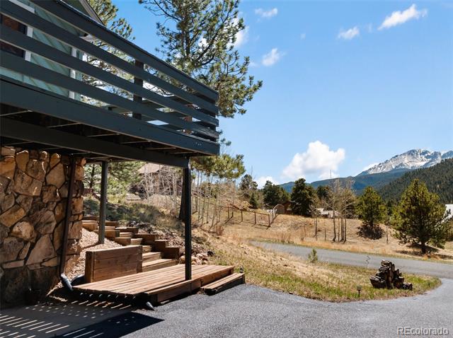 Mountain home with a raised deck and stone walls overlooking mountain peaks.